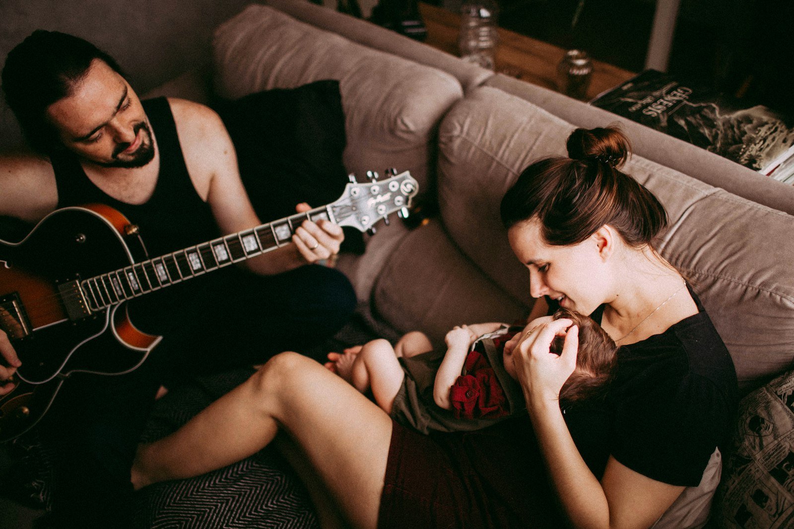 Pais tocando violão e cantando com o bebê no sofá