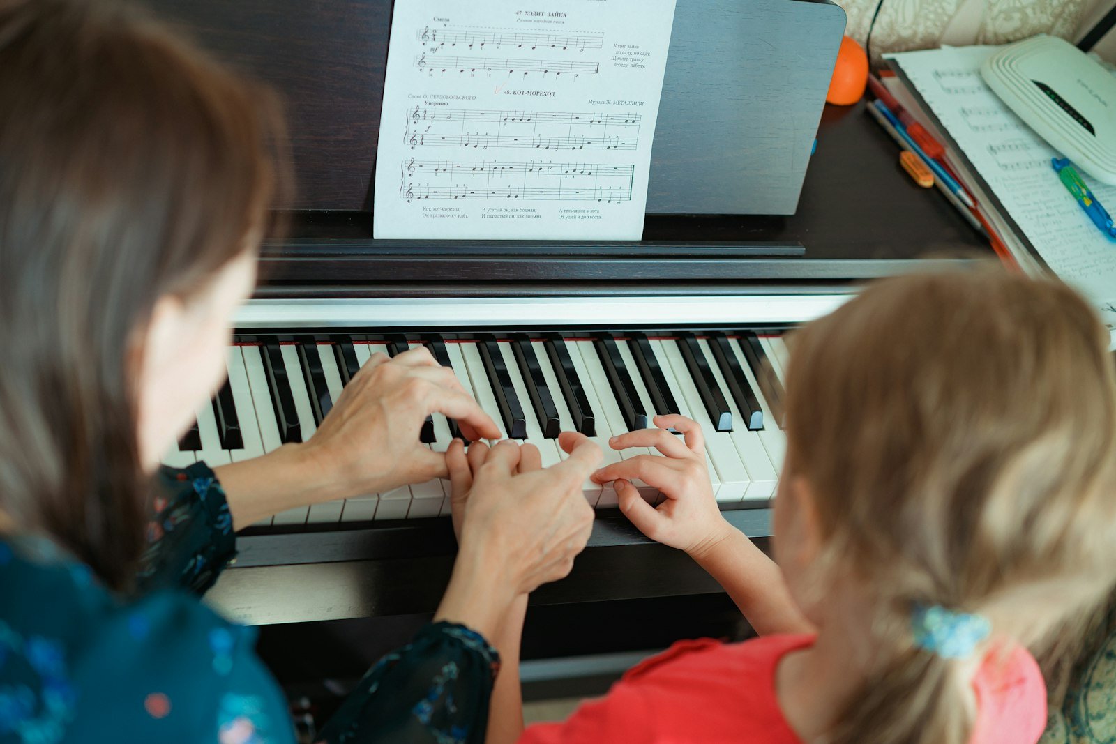 Teacher and young girl playing the piano side by side